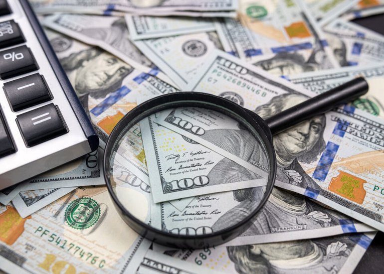 magnifying-glass-on-pile-of-us-dollar-money-banknotes-with-calculator-isolated-on-wooden-table-tax-and-refund-search-or-financial-report-review-concept-1024x683