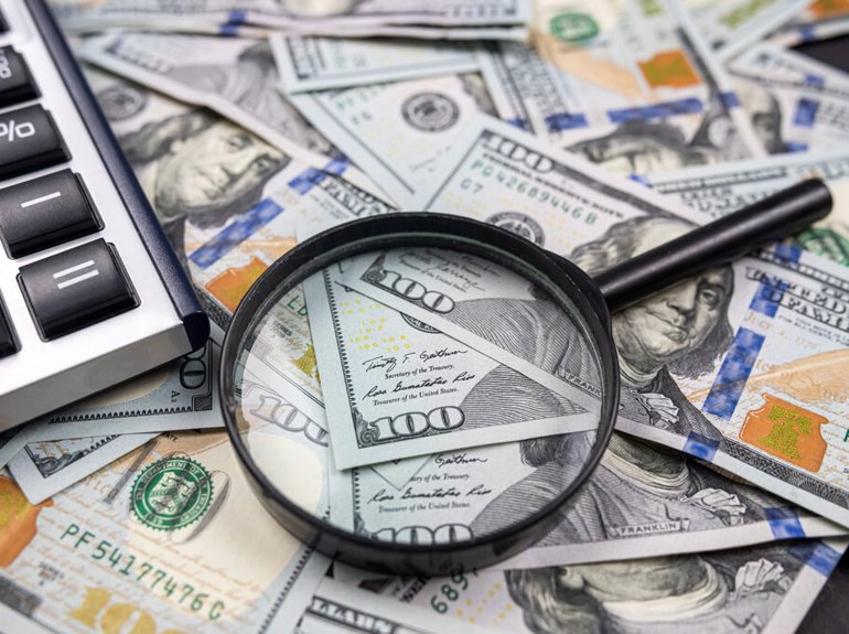 magnifying-glass-on-pile-of-us-dollar-money-banknotes-with-calculator-isolated-on-wooden-table-tax-and-refund-search-or-financial-report-review-concept-1024x683